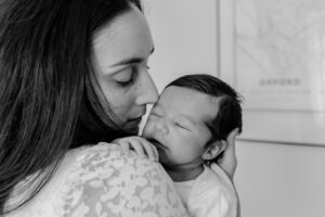 Jess holding newborn baby by her shoulder. Baby is dozing with closed eyes.