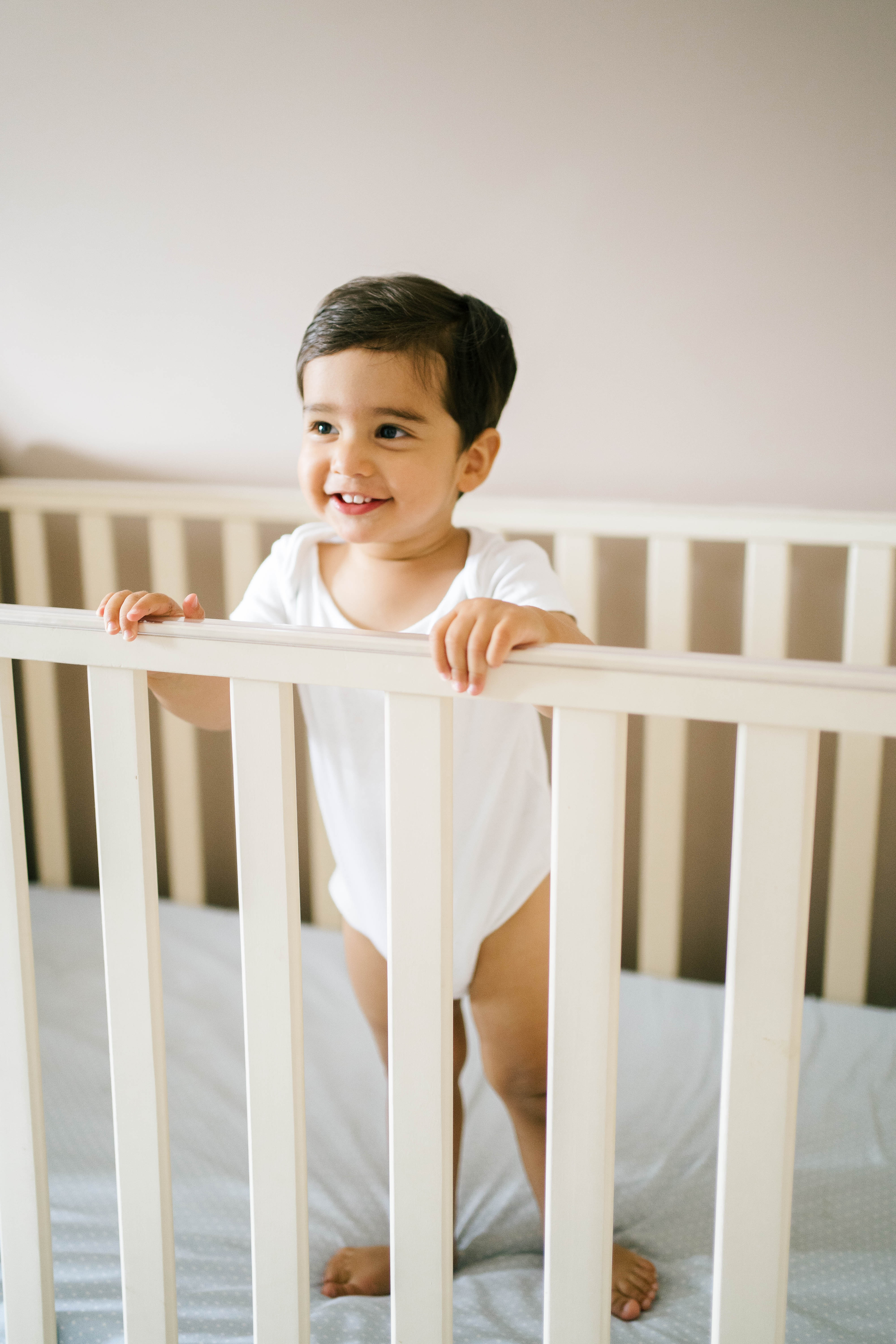 Happy smiling toddler-aged boy standing up inside his crib