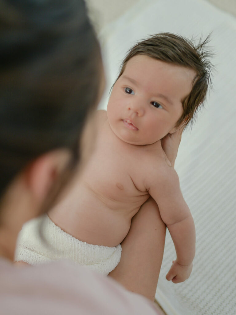 Over-the-shoulder of Mum with content baby smiling up at her