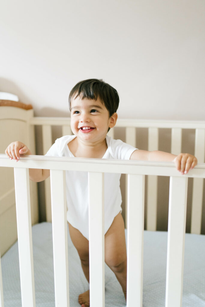 Happy smiling toddler-aged boy standing up inside his crib